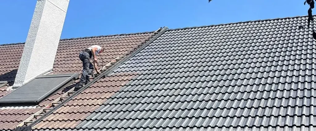 Couvreur réalisant le démoussage et le nettoyage d’une toiture en tuiles à Versailles (Yvelines), avec échelle de toit et assurage.