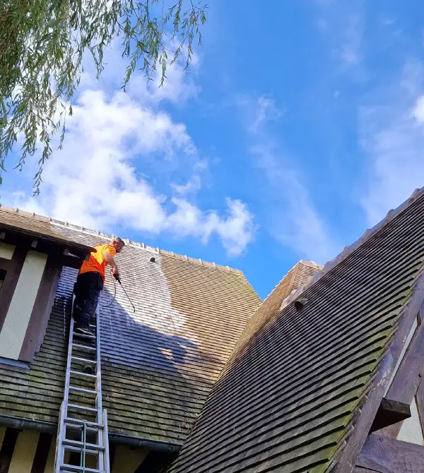 Couvreur nettoyant une toiture en pente au jet contrôlé depuis une échelle, zone claire visible, intervention à Versailles (Yvelines)
