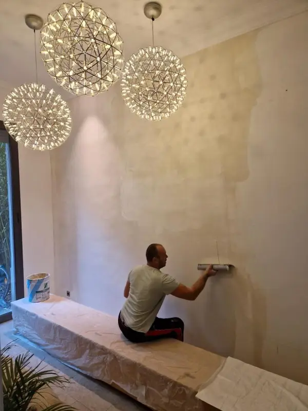 Ravalement et peinture intérieur - extérieur 3 Artisan appliquant une peinture au rouleau sur un mur intérieur protégé par bâches, chantier à Versailles (Yvelines).