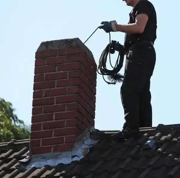 Ramonage 1 Couvreur effectuant le ramonage d’une cheminée en briques sur un toit à Versailles dans les Yvelines.